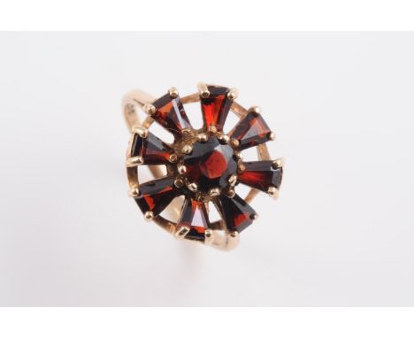 A 9CT YELLOW GOLD AND GARNET SET RING, the abstract open mount set with a round cut garnet within a surround of eight fancy c