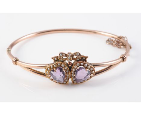 AN AMETHYST AND SEED PEARL BANGLE, the two heart cut amethysts each set within a surround of seed pearls beneath a bow shaped