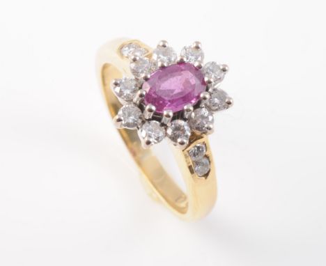 A PINK TOPAZ AND DIAMOND SET RING, the oval cut pink topaz set within a surround of ten brilliant cut diamonds between solid 