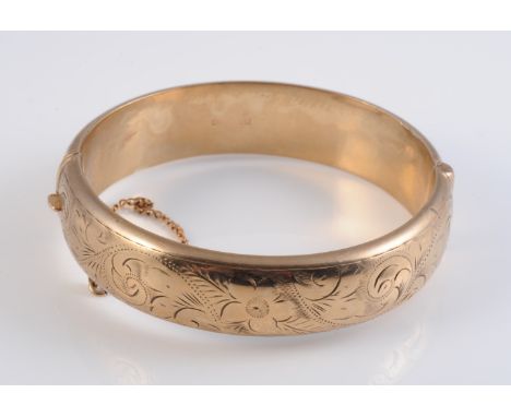A 9 CARAT GOLD HINGED BANGLE, partially engraved with scrolling foliage. 26 grams