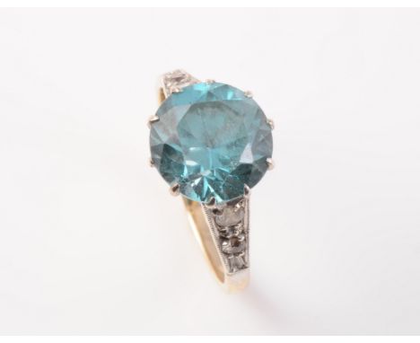 A BLUE ZIRCON SET RING, the round cut blue zircon claw set in a pierced mount between pierced tapering shoulders each set wit