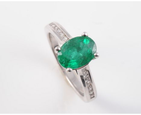 AN 18CT WHITE GOLD, EMERALD AND DIAMOND RING, the oval cut emerald claw set raised in an open mount between open tapering sho