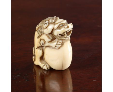 A JAPANESE IVORY NETSUKE, Meiji period, carved as a dog of foo on a ball. 36mm