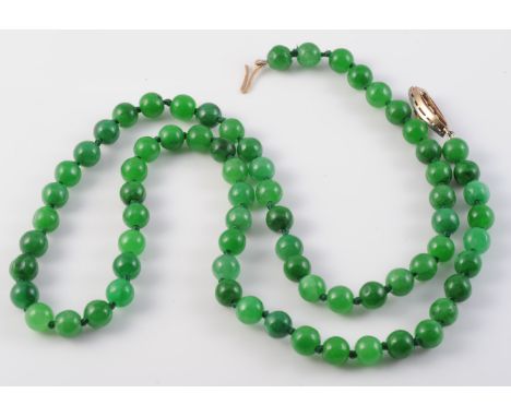 A JADEITE BEAD NECKLACE, the seventy uniform jadeite beads strung knotted onto an integral tongue clasp set with a single pea