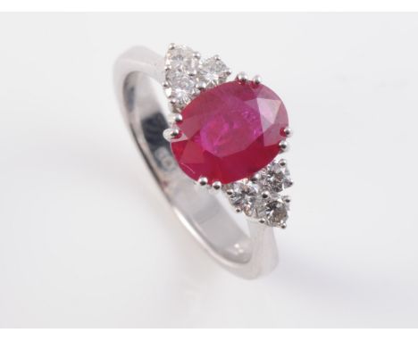 AN 18CT WHITE GOLD, RUBY AND DIAMOND RING, the oval cut ruby claw set between three brilliant cut diamond highlights to each 