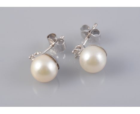 A PAIR OF CULTURED PEARL AND DIAMOND EAR STUDS, the single cultured pearl set simply beneath a single brilliant cut claw set 