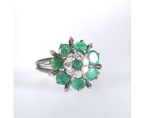 AN EMERALD AND DIAMOND CLUSTER RING, the central emerald within a surround of seven diamonds further within seven emeralds wi