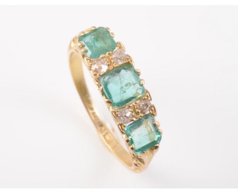 A LATE 19TH CENTURY EMERALD AND DIAMOND RING, the three graduating square cut emeralds set in a pierced and delicately scroll