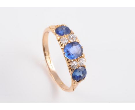 A MID VICTORIAN SAPPHIRE AND DIAMOND RING, the three graduating oval sapphires set in a subtle pierced and scrolling detailin