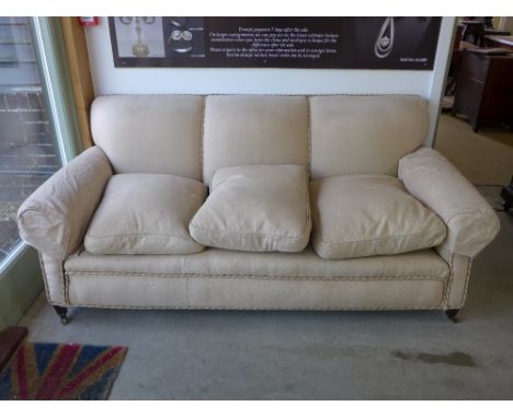 An early 1900's Howard and Sons three seater sofa on short tapering mahogany feet and brass castors stamped HOWARD & SONS LTD