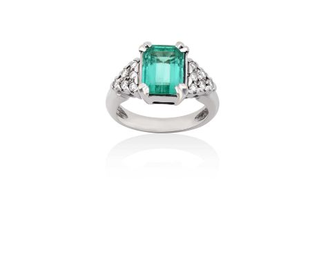 An Emerald and Diamond Ringthe emerald-cut emerald in a white claw setting, to round brilliant cut diamond set shoulders, on 