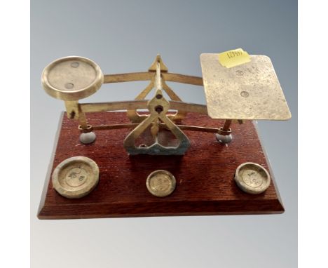 A set of antique brass postal scales and weights mounted on a board.