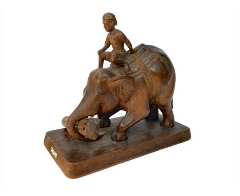 BURMESE CARVED TEAK MODEL OF AN ELEPHANT AND RIDER, the elephant holding a log in its trunk, with a rectangular wood base, 25
