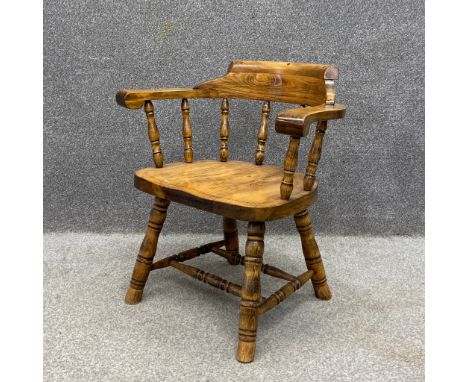 An  elm bow smoker's armchair having a curved and scrolled top rail and arms on eight turned spindles over a shaped saddle se