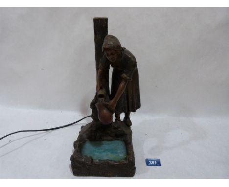 An early 20th century cold painted metal figure of a woman collecting water, the glass pool illuminated by an electric light 