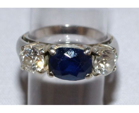 A 3 stone dress ring set with an oval central sapphire flanked by 2 diamonds, on white metal shank (unmarked)