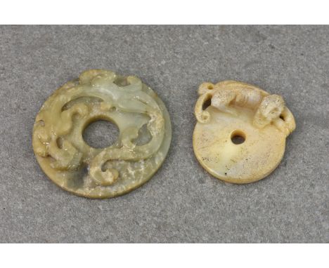 Two Chinese carved jade Pi discs, probably 19th century, the larger in shaded green jade, having raised carving of mythical b