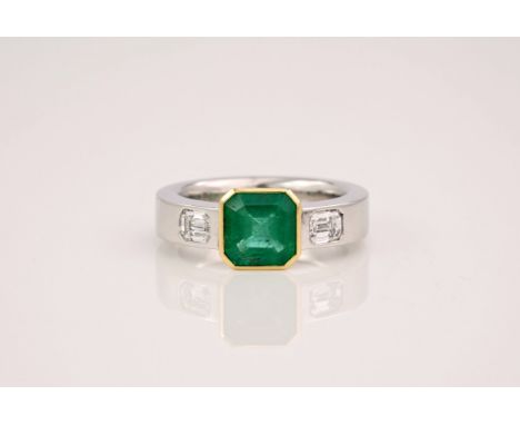 An 18ct white gold, emerald and diamond three stone ring, the central emerald of 1.9ct with two emerald cut diamonds either s