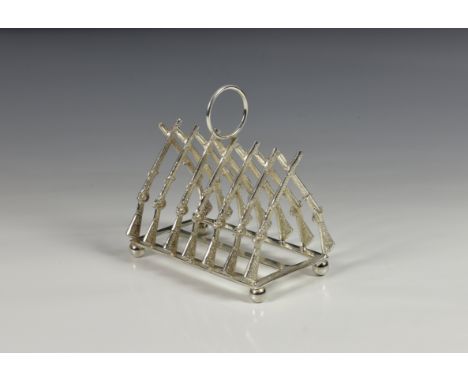 A modern silver plate novelty six division toast rack fashioned as crossed rifles, with central ring handle, raised on ball f