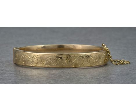 A 9ct hollow yellow gold hinged bangle, with foliate and scrolled engraving details to the top half. Approximately 61mm in di