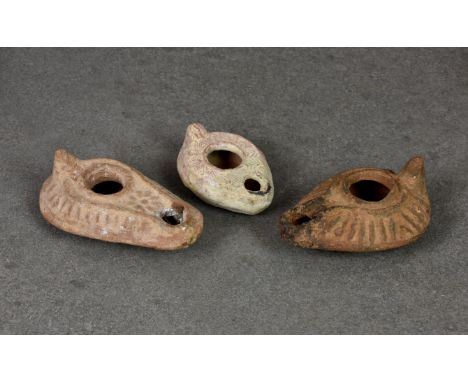 Three Roman terracotta oil lamps, two of teardrop form with peaked handle and raised line decoration, one with flowerhead on 