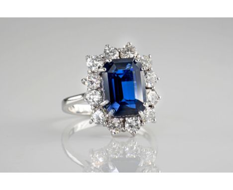 An 18ct white gold, sapphire and diamond cluster ring, the central, emerald cut sapphire of deep, blue colouring, measuring a