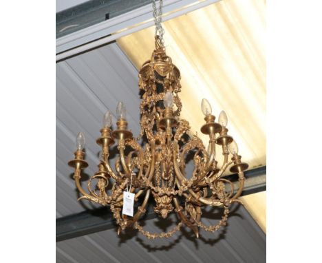 A Gilt Metal Twelve-Light Chandelier, in Louis XVI style, with scroll cresting over foliate swag and drop mounted baluster st