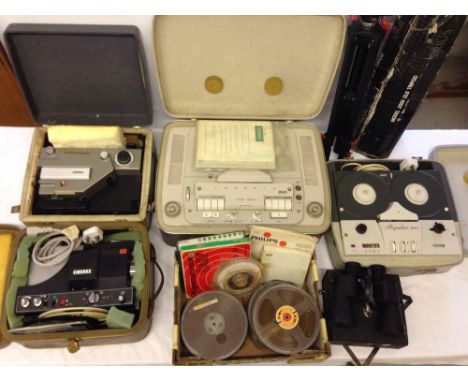 A quantity of c1960s cine projectors and reel to reel machines with a cased pair of binoculars and a camera tripod.