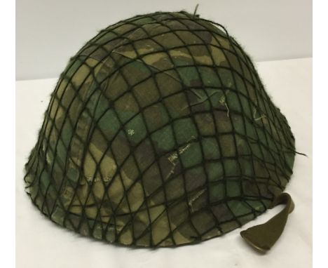 A British Army helmet with liner, camoflage cover and net. Liner bears date for 1981.