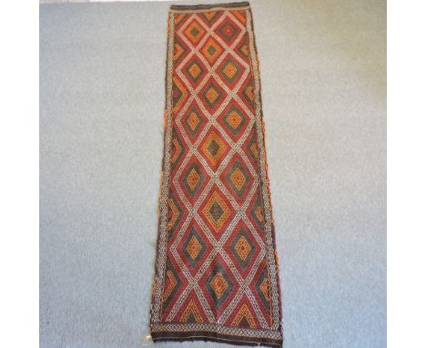A Persian kelim runner, with all over geometric design, on a red ground, 292 x 80cm