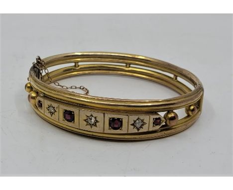 A late 19th century precious yellow metal hinged bangle set garnets and diamonds, having three illusion set old-cut diamonds 
