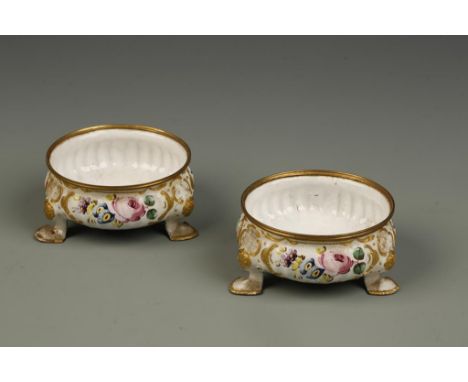 A PAIR OF "BATTERSEA" ENAMEL SALTS with gilt metal rims and painted with flowers in raised gilt scroll borders, on white grou