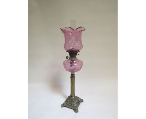 A Victorian oil lamp the etched cranberry shade and reservoir over reeded brass column to pierced base