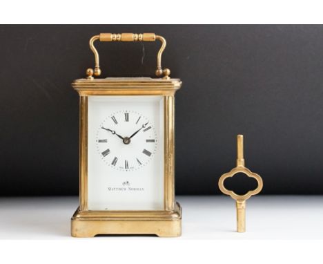 A brass cased carriage clock with bevelled glass panels, white enamel dial with retailers mark 'Matthew Norman', complete wit