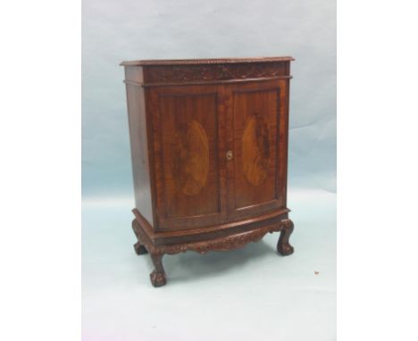 An Edwardian bow-fronted mahogany cupboard, pair of flame-veneered panelled doors enclosing single shelf, carved leaf-scroll 