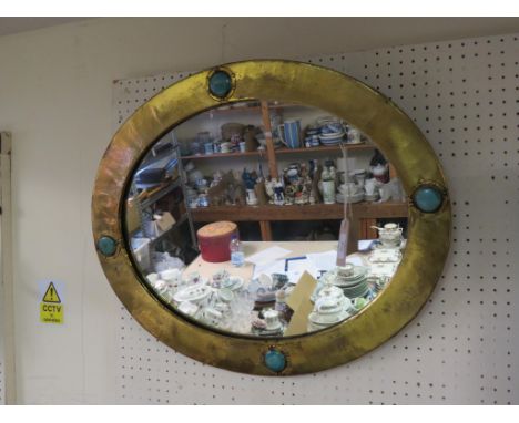 A Liberty & Co. hammered brass mirror, oval-shape, frame inset with ceramic blue-green bosses, labelled and dated verso, 1906