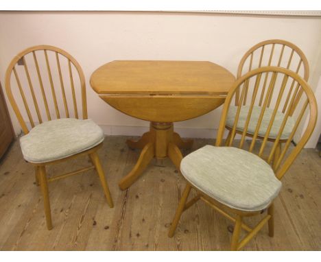 A modern light wood drop-leaf dining table, on pedestal base, and three stick-back dining chairs