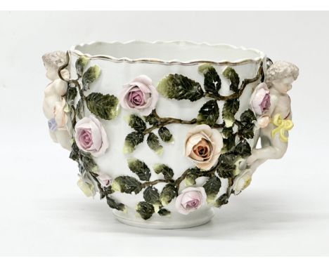 Sitzendorf, Germany. C.1900. A flower encrusted jardiniere. With twin putti’s holding vines and leaves on a glazed white grou