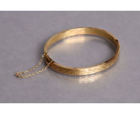 An un-marked yellow metal stiff hinged bangle with engraved decoration (11.8g).