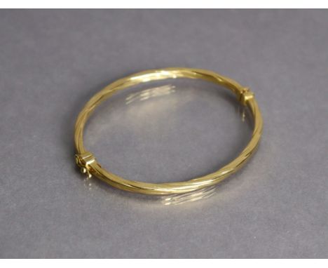 An 18ct yellow gold stiff hinged bangle with sprung hinge &amp; rope-twist design (6.9g).
