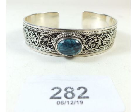 A white metal bangle with scrollwork decoration and set turquoise