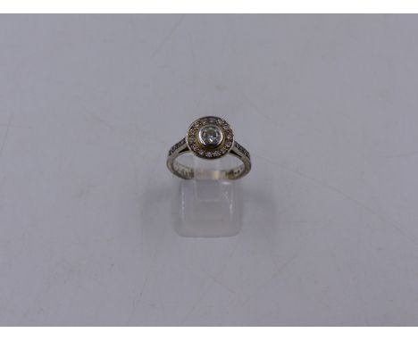 A PRECIOUS WHITE METAL DIAMOND SET HALO RING STAMPED ROYAL. THE CENTRAL BRILLIANT CUT DIAMOND IS IN A RUBOVER SETTING, SURROU