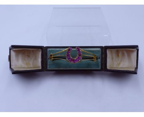 A 15ct STAMPED RUBY AND DIAMOND HORSESHOE HINGED BANGLE, COMPLETE WITH SAFETY CHAIN AND FITTED CASE. THE HORSESHOE IS SET WIT