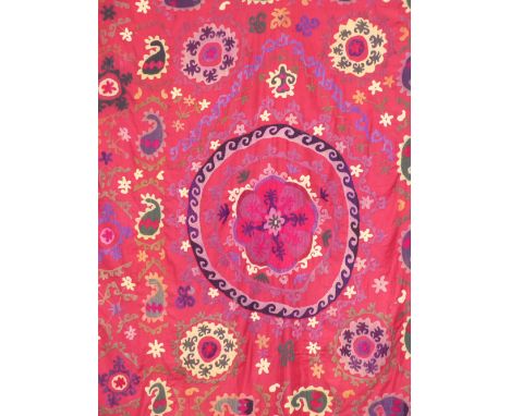 A Suzani needlework panel central medallion surrounded by scrolling motifs on a red field