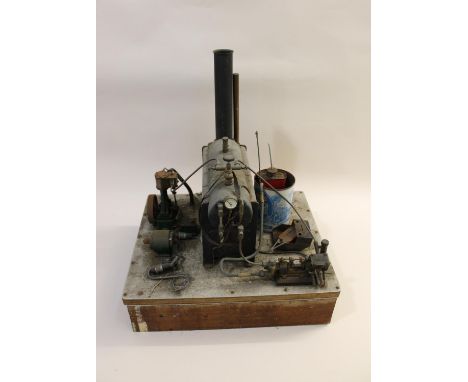 A large Stuart boiler with pressure gauge operating a range of attachments including a fly wheel, mounted on a wooden plinth.