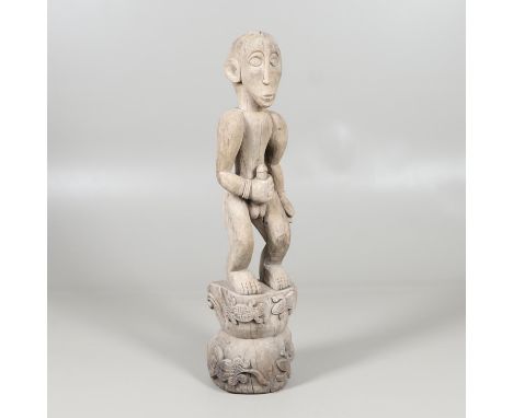 A large carved figure holding his genitalia, the figure standing on a tree stump and carved with animals around the base. 121