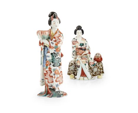 TWO PORCELAIN FIGURES OF A GEISHAMEIJI PERIOD the first figure shown seated beside a Daruma doll on a bench draped with a clo