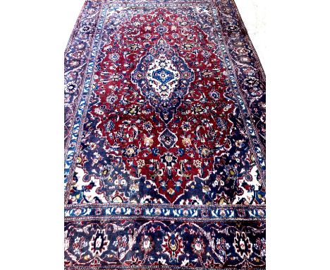 Red and blue ground Persian Kashan carpet with traditional floral designs.  285x176cm approx.  (B.P. 21% + VAT) 