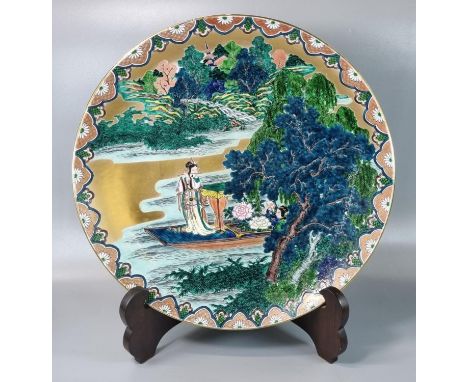 Japanese porcelain Kutani polychrome charger depicting a woman on a boat playing a flute in a landscape, painted in predomina