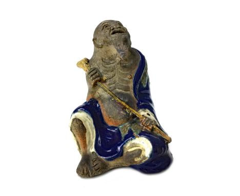 EARLY 20TH CENTURY JAPANESE SUMIDA FIGURE, modelled as a seated male holding a pipe-like instrument, 12cm high